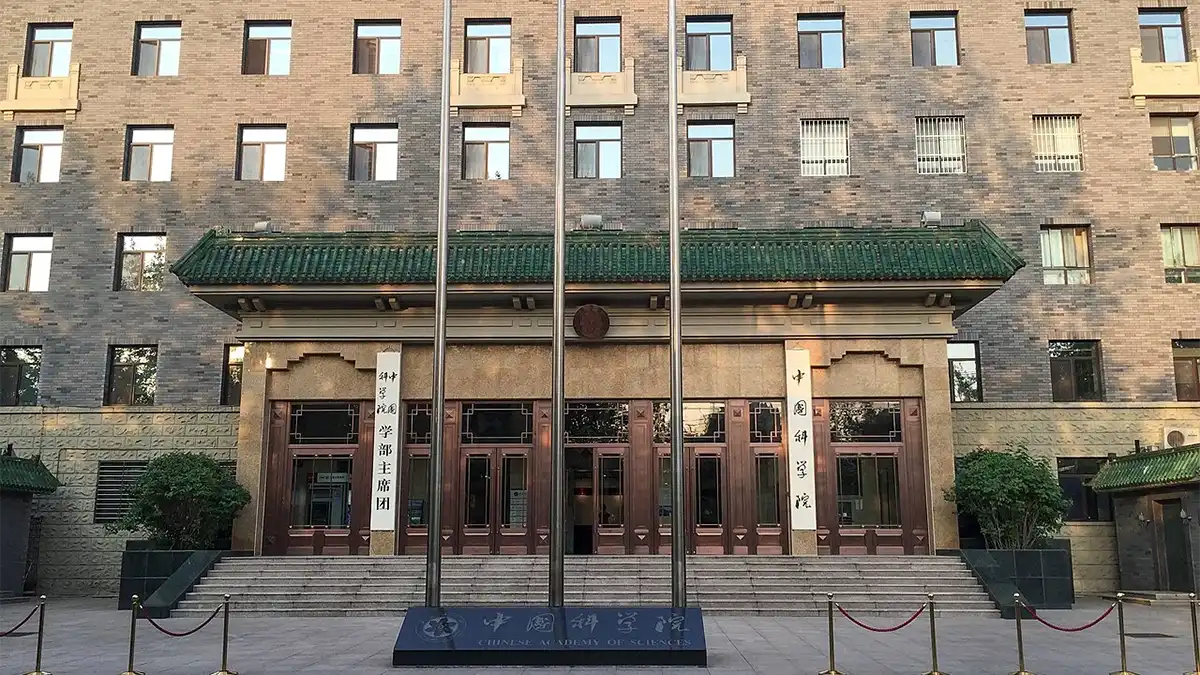 Brick facade of the Chinese Academy of Sciences building with green tiled roof, large wooden doors, three flagpoles, and decorative signage.
