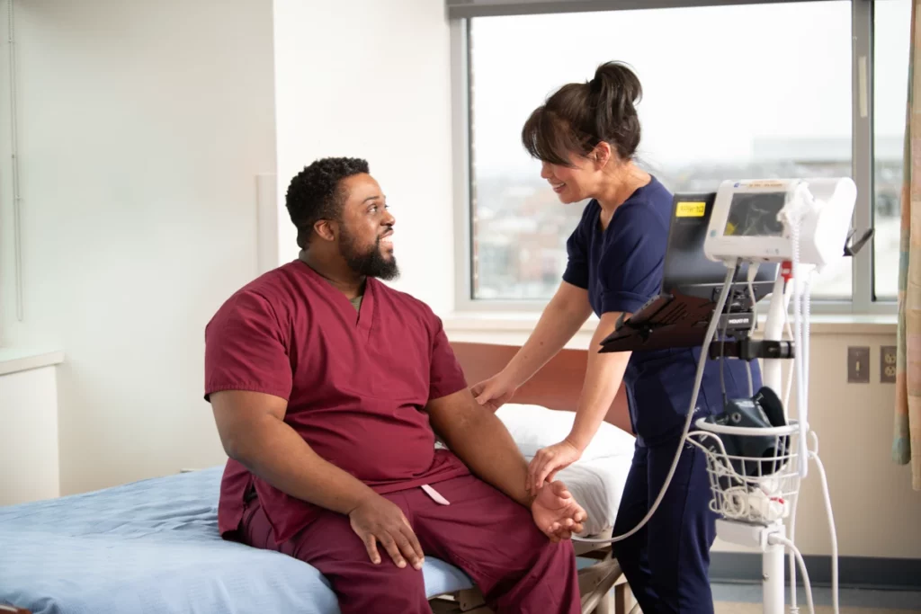 Clinician checks a participant’s vitals during clinical trials in a hospital room setting with monitoring equipment nearby.