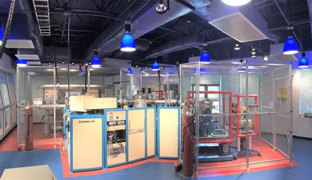 A high-tech laboratory featuring a SSAMS50 accelerator mass spectrometer surrounded by equipment and safety cages, used for precise isotope analysis.