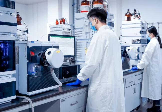 Scientists in lab coats and protective gear operate advanced equipment, conducting research in analytical and purification sciences. Machines and computers analyze samples in a controlled laboratory environment.
