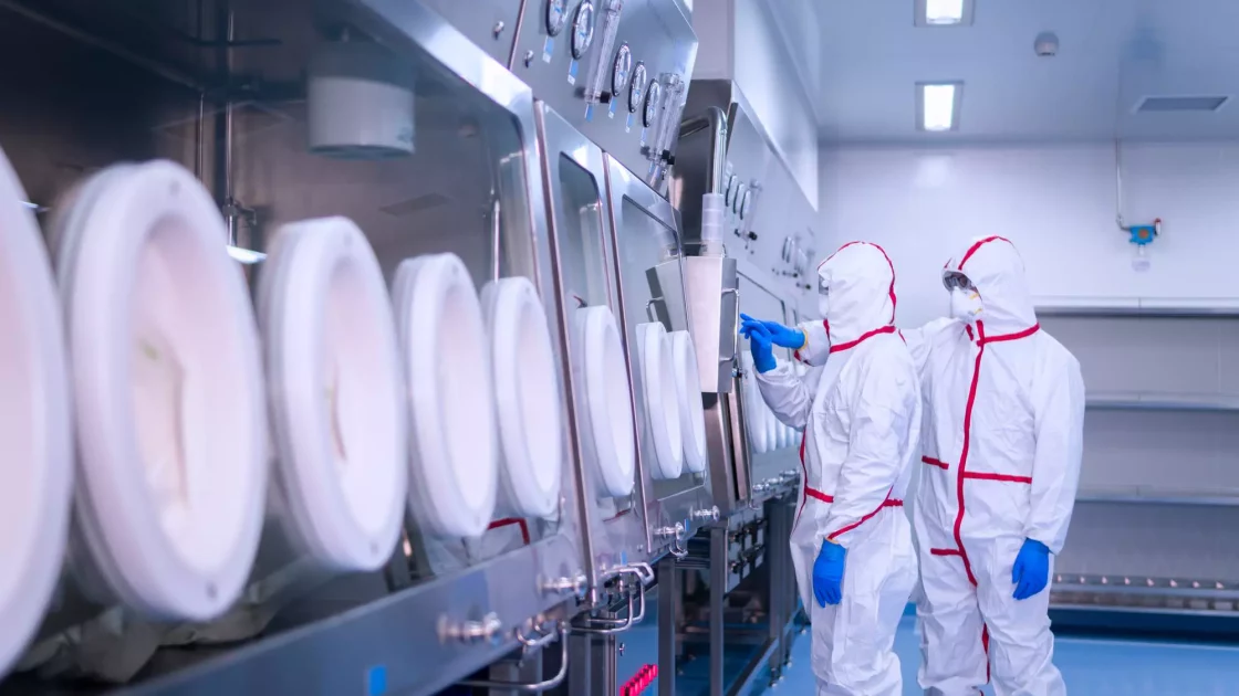 Two workers in full protective gear operate equipment inside an advanced API manufacturing facility, using an isolator system for handling materials.