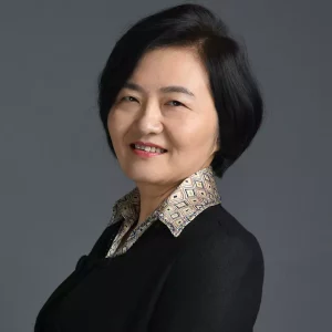 Bei Zheng - A woman with short black hair, wearing a black blazer over a patterned collared shirt, smiles at the camera. The background is a neutral gray, adding a touch of professionalism to her expertise in genetic toxicology.