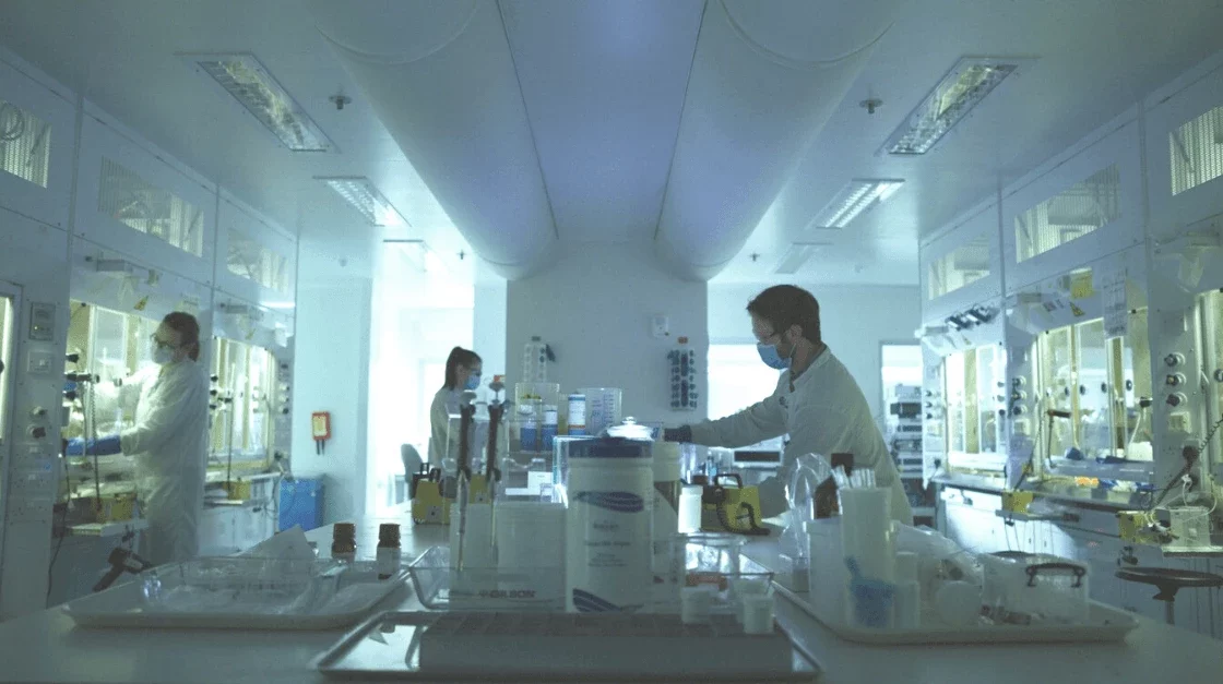 Scientists in a sterile lab environment conduct Carbon-14 radiosynthesis experiments, using fume hoods and advanced equipment for safe handling.