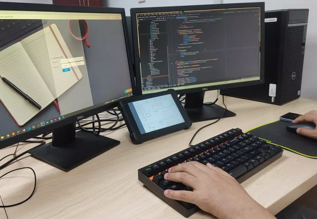 A scientist works on a dual-monitor setup, coding algorithms related to chemometrics. One screen shows code, while the other displays a digital notebook login. A tablet nearby presents molecular structures.