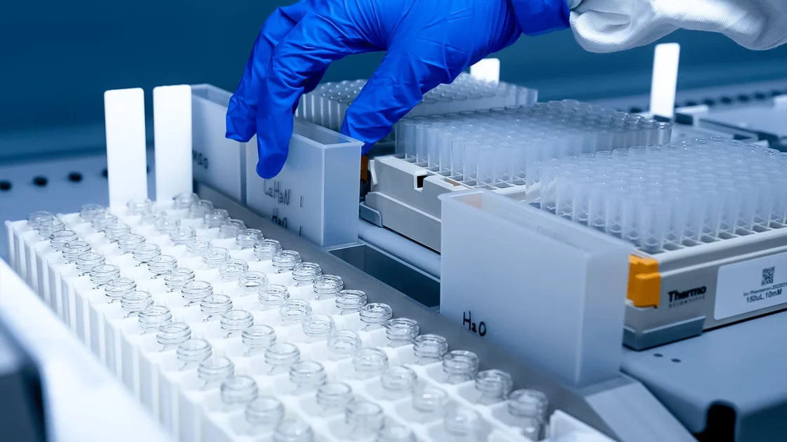 Gloved hand organizing vials in a compound management system, preparing samples for storage or testing in a lab environment.