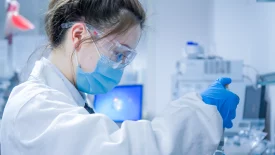 A scientist in protective gear uses a pipette in a laboratory, performing Discovery in vivo pharmacokinetics (PK) research with analytical equipment in the background.