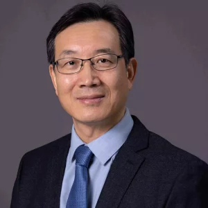 Dr.-Boliang-Lou - A man with short black hair, glasses, and a gentle smile is wearing a dark suit, blue dress shirt, and blue tie. The background is solid gray, reminiscent of the precision found in preclinical ADME studies.