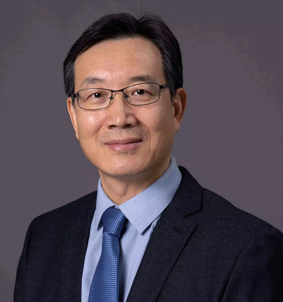 Dr.-Boliang-Lou - A man with short black hair, glasses, and a gentle smile is wearing a dark suit, blue dress shirt, and blue tie. The background is solid gray, reminiscent of the precision found in preclinical ADME studies.