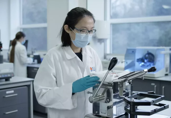 A scientist in protective gear operates equipment for tablet compression in a lab, focusing on formulation development processes.