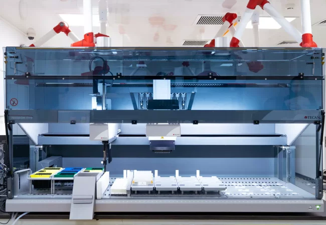 The image shows a sophisticated laboratory automation device, likely a robotic liquid handling system designed for preclinical ADME studies. It features trays with various colored containers, a robotic arm, and multiple pipettes, all housed in a sleek, transparent enclosure.