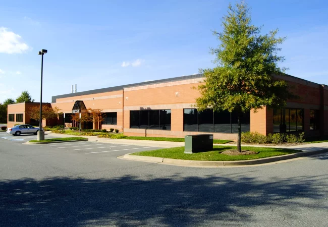 A brick office building with large tinted windows, surrounded by a parking lot and landscaped greenery, located at the Germantown site.