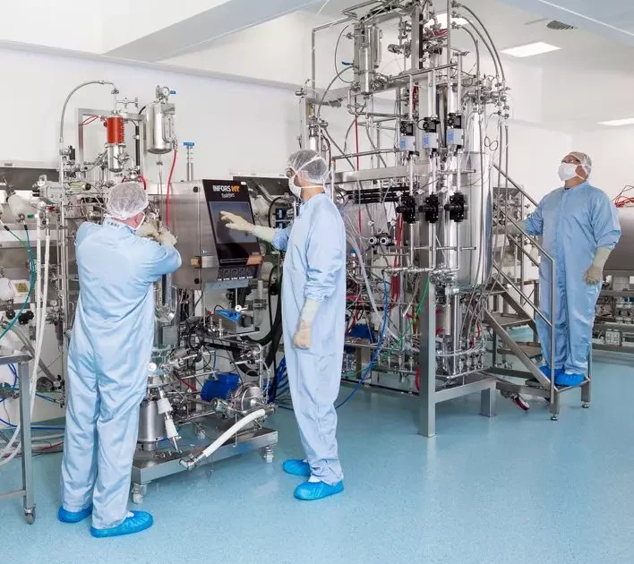 Scientists in full protective gear operate advanced bioreactor systems for GMP and research-grade plasmid manufacturing in a cleanroom facility.