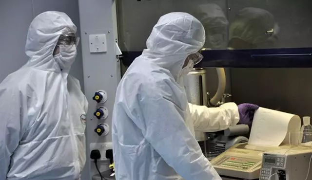 Two scientists wearing full protective suits and goggles operate machinery in a controlled lab environment, emphasizing safety and precision in scientific processes.