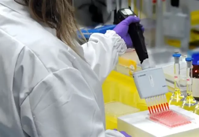 A scientist in a lab coat and gloves uses a multichannel pipette to dispense radiolabeled compounds into a 96-well plate for in vitro metabolism studies.