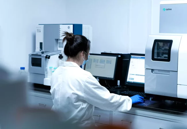A scientist uses Cytiva lab equipment and a computer to conduct in vitro biology experiments, analyzing biological samples for research.