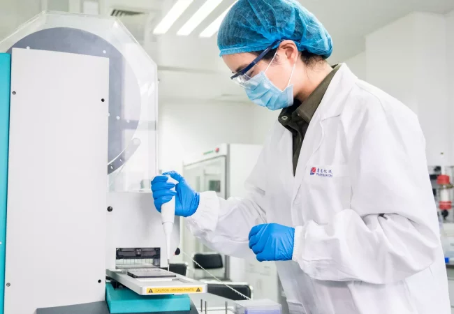 A scientist using a pipette and automated equipment to perform in vitro disease biology research in a controlled lab environment.