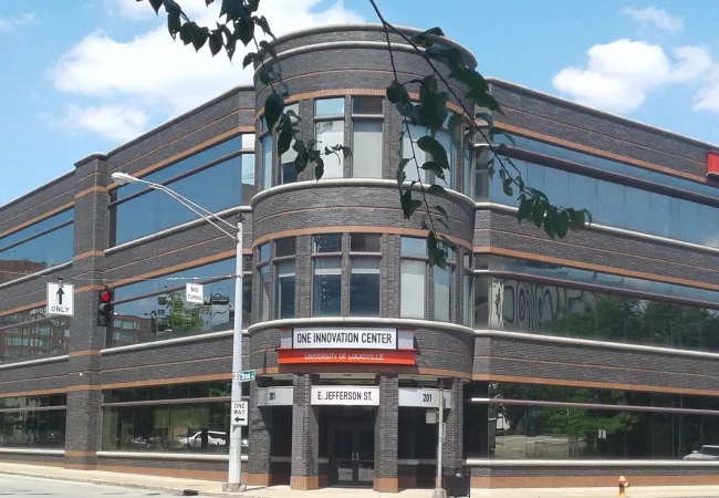 A modern glass and brick building labeled "One Innovation Center" at the University of Louisville, located at the corner of E. Jefferson Street.