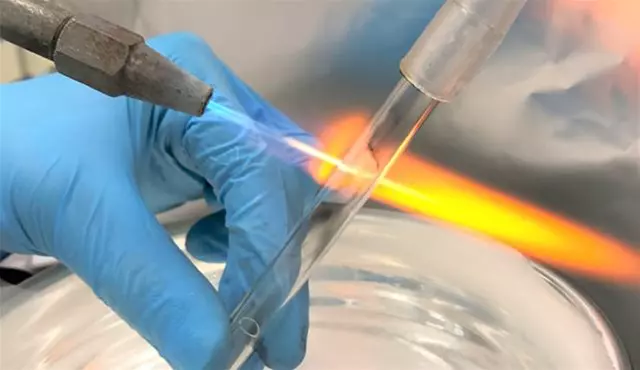 Scientist using a blue flame to seal a glass tube, part of a sample preparation process for mass balance analysis with AMS.