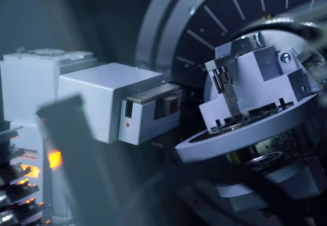 Close-up of advanced material science equipment analyzing a sample, with precise mechanical arms and illuminated components in a high-tech setting.