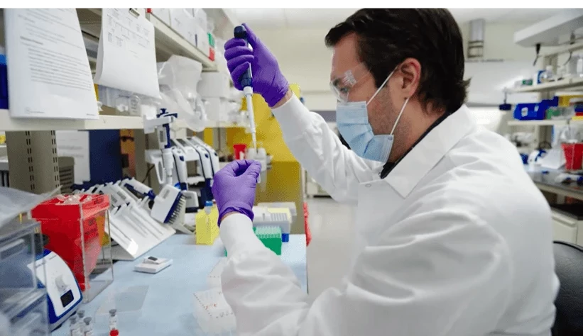 A scientist in protective gear uses a pipette to prepare samples for metabolite profiling with accelerator mass spectrometry (AMS) in a well-equipped laboratory.