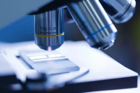 A close-up of a microscope with a 10x objective lens focuses on a slide, indicating a pathology analysis. The softly lit, sterile environment highlights detailed cellular examination.