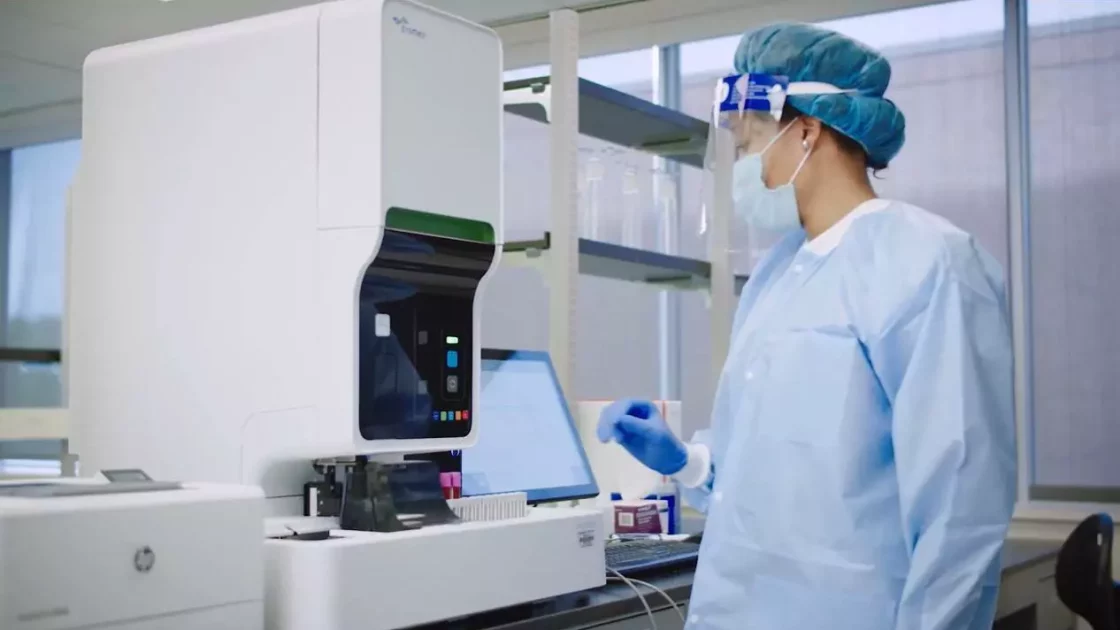 Scientist in protective gear operates advanced lab equipment for pharmacokinetics analysis using radiolabeled compounds.