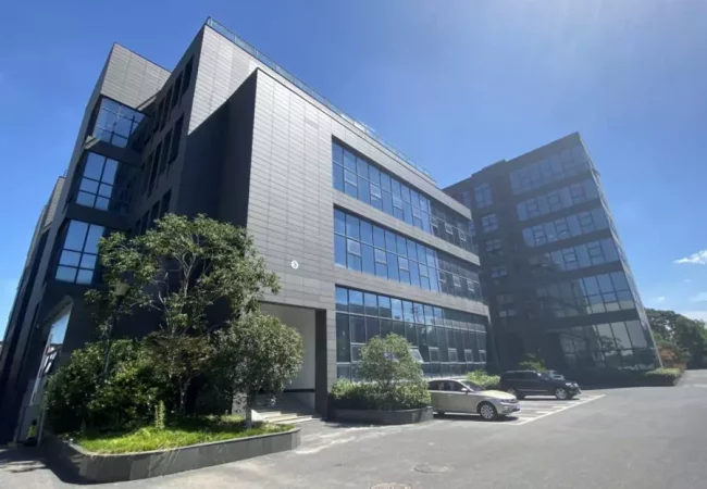 The Pharmaron Nanjing site, a modern glass and steel building under clear skies, features greenery and parked cars in its surroundings.