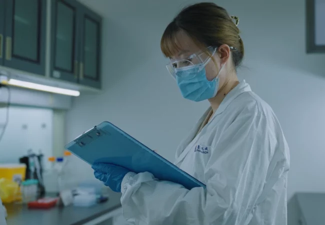 A scientist in safety gear reviews data on a clipboard in a lab, conducting general toxicology assessments for pharmaceutical studies.