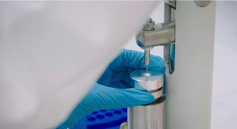 A gloved scientist handling a sample in a precise metal holder, preparing for mass balance analysis using Accelerator Mass Spectrometry (AMS).