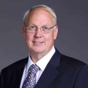 Stephen Lewinton - A smiling man with short, light hair and glasses wearing a dark suit, a white shirt, and a patterned tie poses against a plain gray background, embodying the precision of preclinical ADME studies in his meticulous appearance.