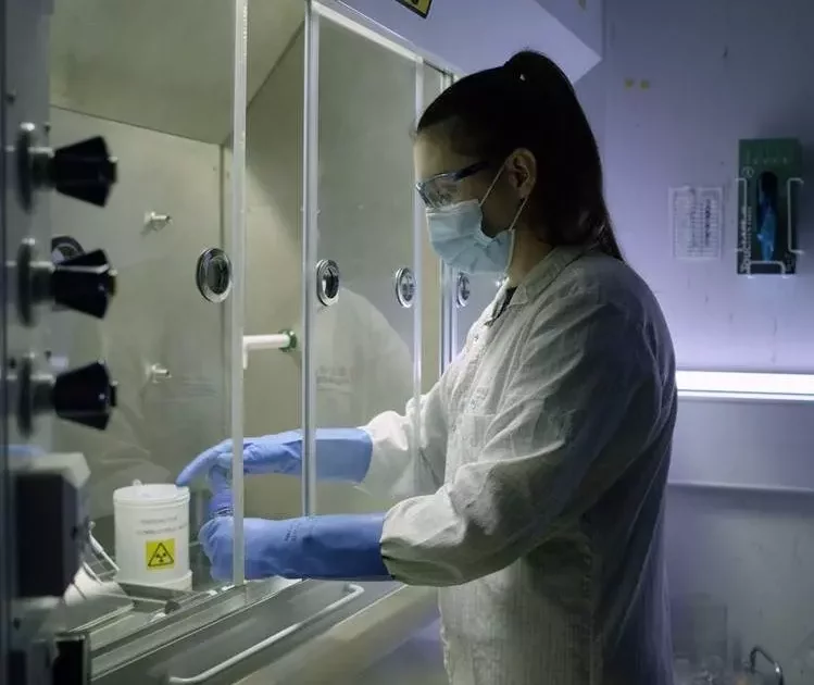 A scientist in protective gear handling tritium radiosynthesis materials inside a radiation safety cabinet, ensuring controlled conditions.