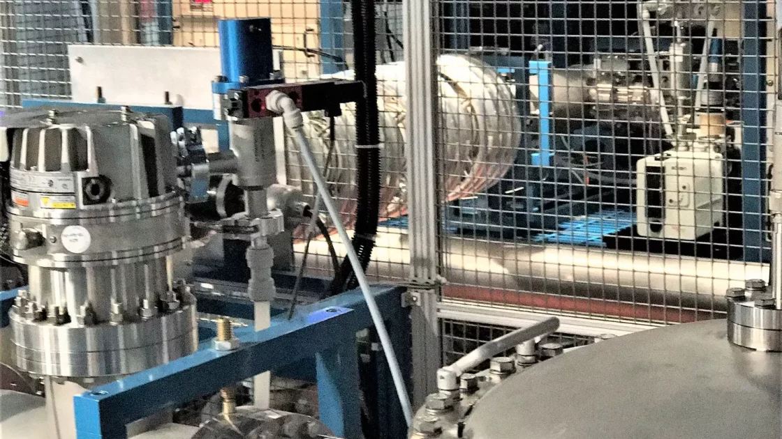 Close-up of ultra-sensitive Accelerator Mass Spectrometry (AMS) equipment, featuring metallic chambers, pipes, and valves enclosed in a protective wire mesh.