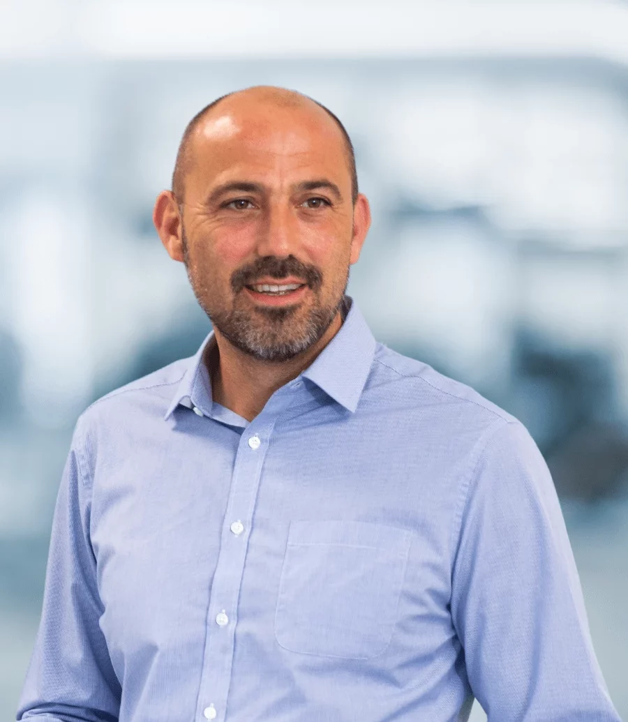 Andrew Evans, Associate Director, Engineering, Pharmaron Gene Therapy. A middle-aged man with a trimmed beard and bald head, wearing a light blue button-down shirt, stands in front of a blurred office background. He has a calm, approachable expression.
