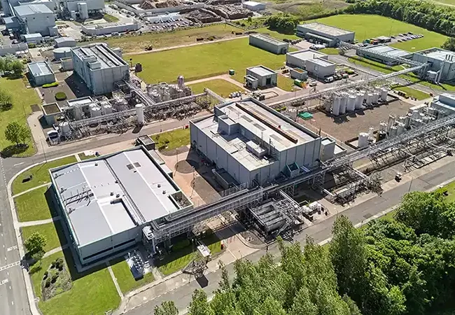 Aerial drone view of Pharmaron Cramlington’s API manufacturing facility, featuring interconnected buildings, pipe racks, and green surroundings.