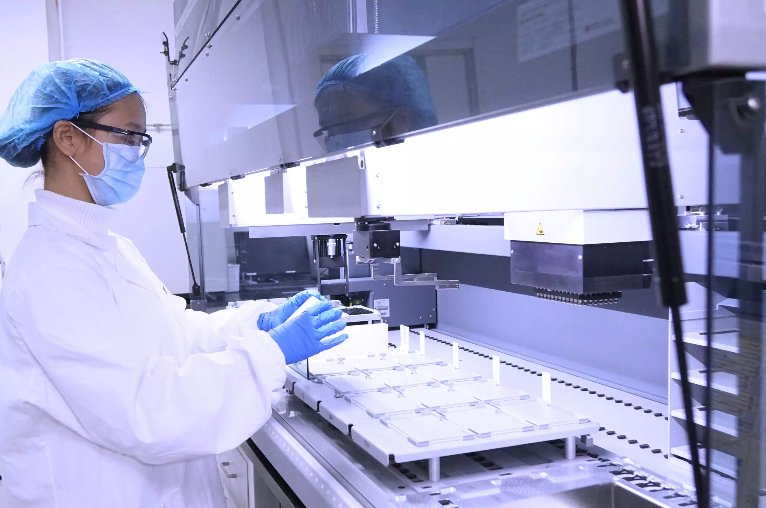 Scientist in full PPE handling samples on a high-throughput automated system in a compound management lab.