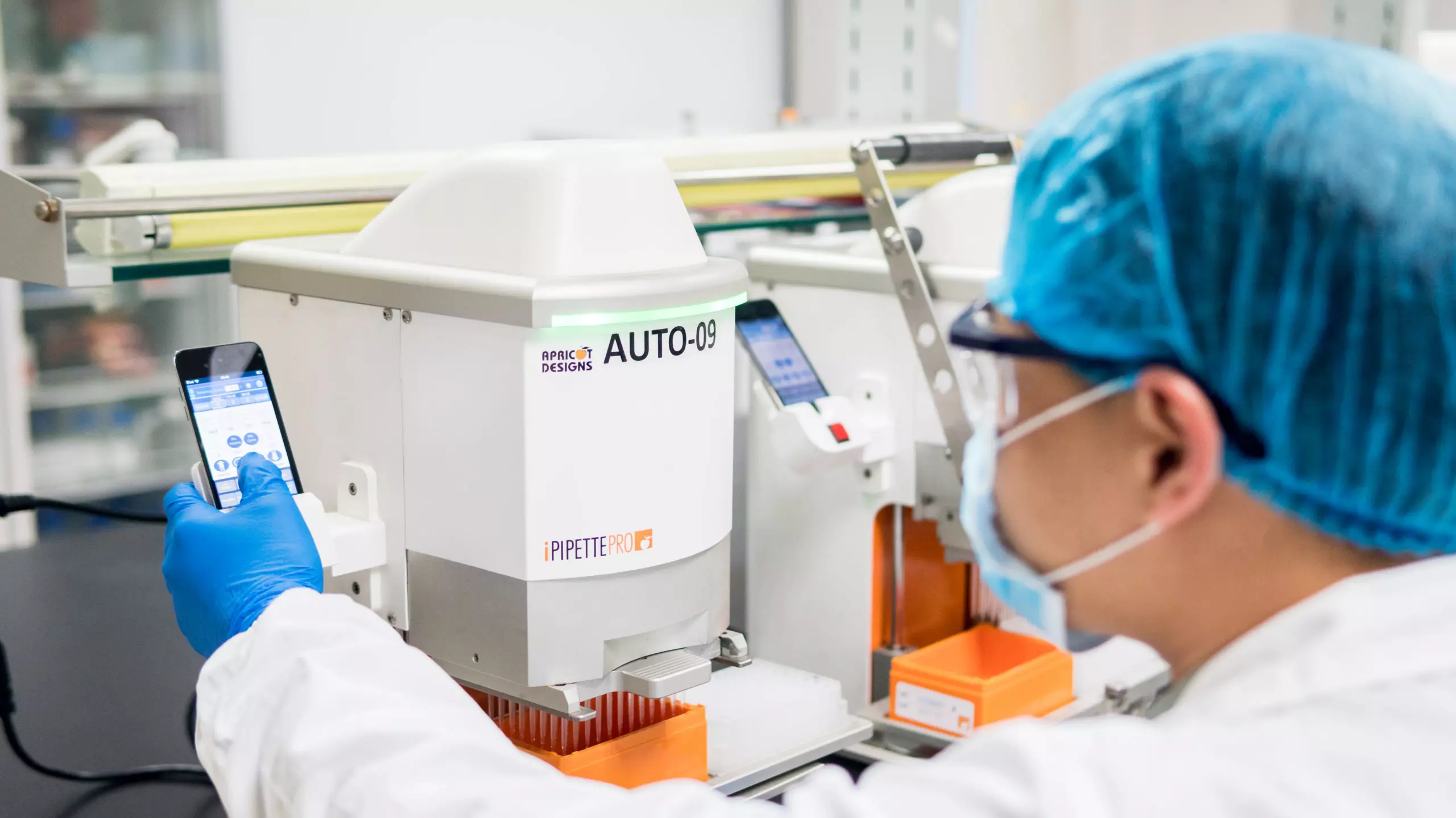 Scientist using an automated pipetting system (AUTO-09) controlled via smartphone in a lab setting for DMPK studies.