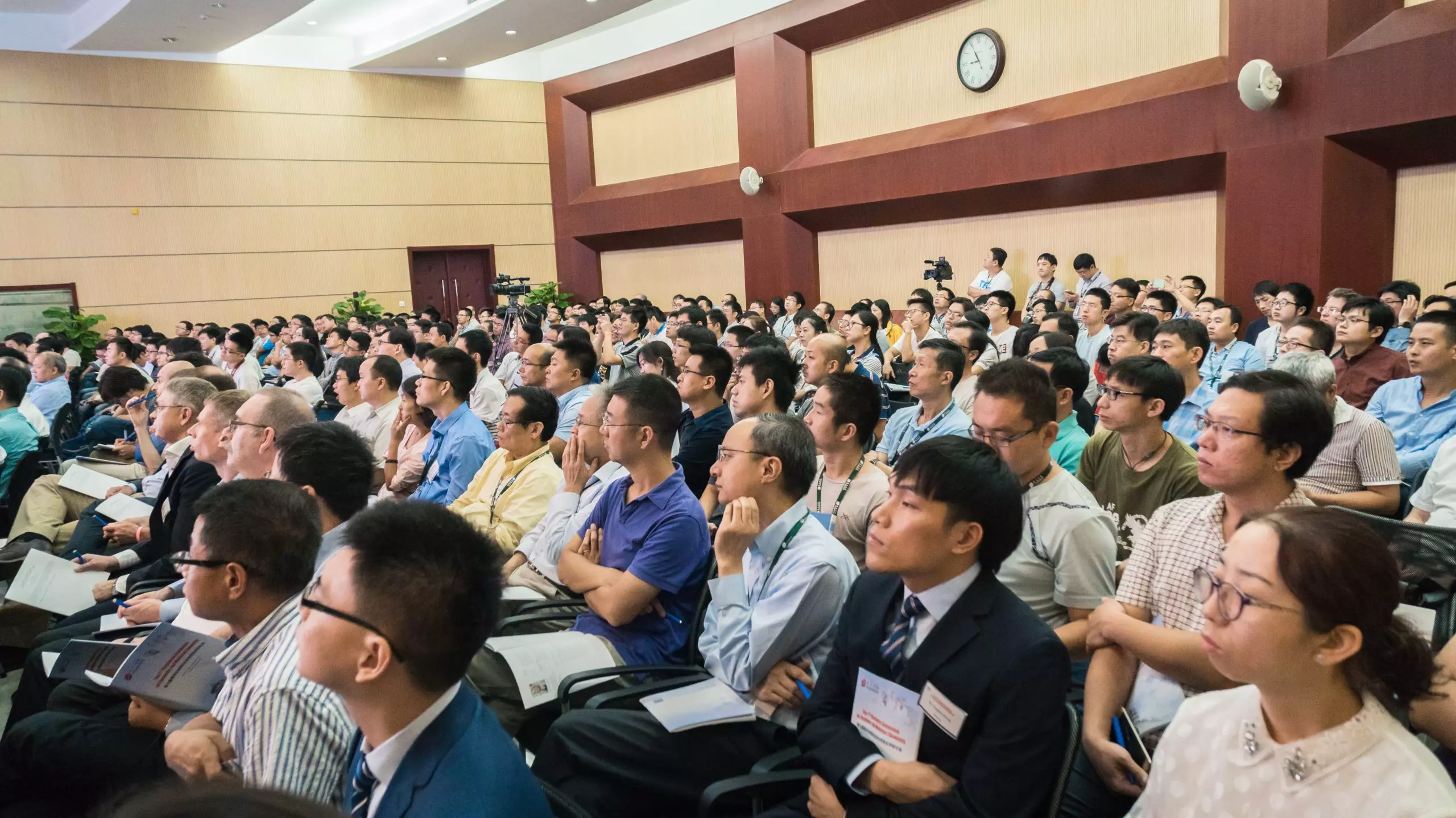 A large audience attentively listens to a presentation in a lecture hall, with people from diverse professional backgrounds engaged in learning.