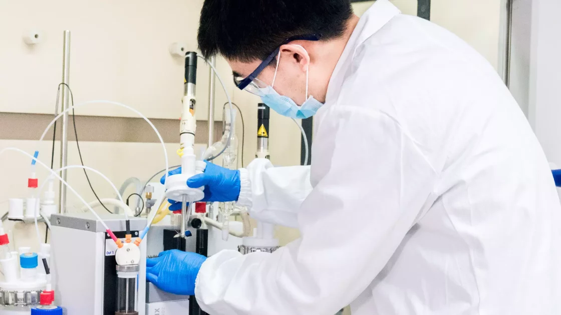 A scientist in protective gear operates lab equipment to measure physical properties during a pre-formulation study, working with various connected devices and tubes.