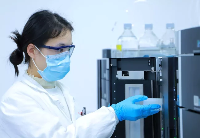 A scientist wearing safety goggles, a mask, and gloves operates advanced lab equipment for regulatory in vivo pharmacokinetic (PK) studies.