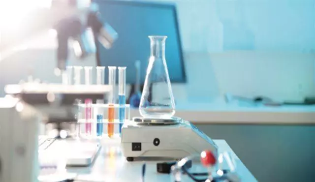 A laboratory setup with a flask on a magnetic stirrer, test tubes filled with colored solutions, and a microscope in the background for radiolabelled metabolism and biodistribution studies.