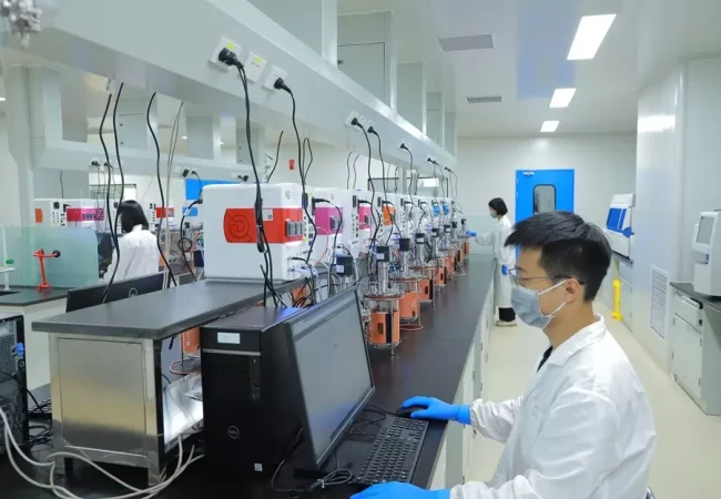 Scientists working in a process development lab, with multiple reactors and bioprocessing units connected to computers, analyzing and optimizing procedures.