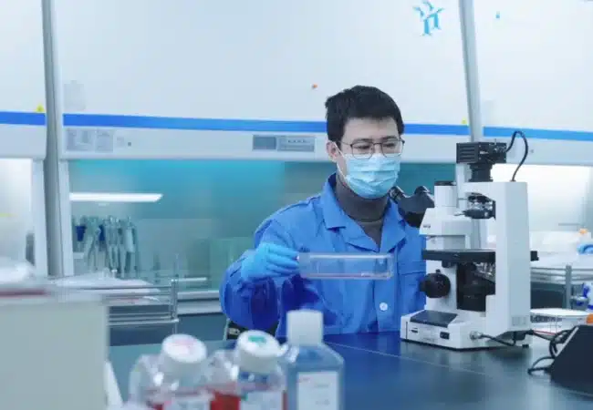 Man in blue lab coat using a cell culture microscope to preform target identification and target validation.