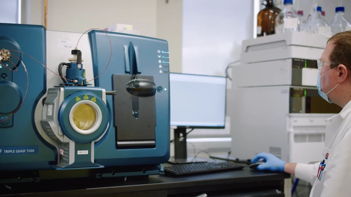 A scientist operates a Triple Quad 5500 mass spectrometer in a preclinical bioanalysis lab, analyzing large molecules for drug development research.
