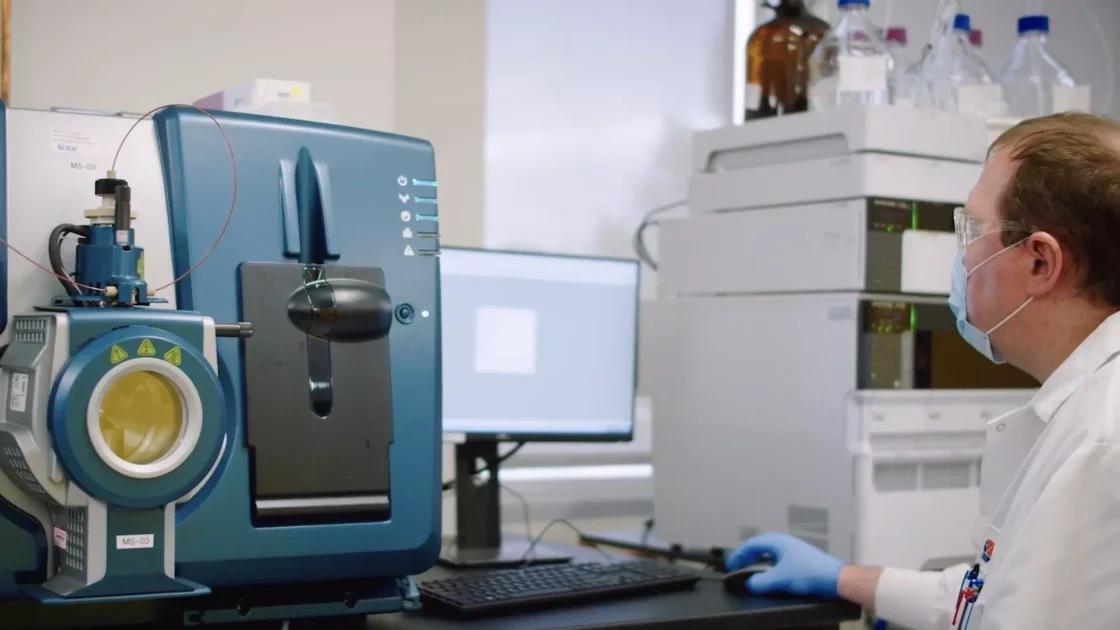 A scientist operating advanced analytical equipment, performing preclinical bioanalysis of small molecules with a mass spectrometer setup.