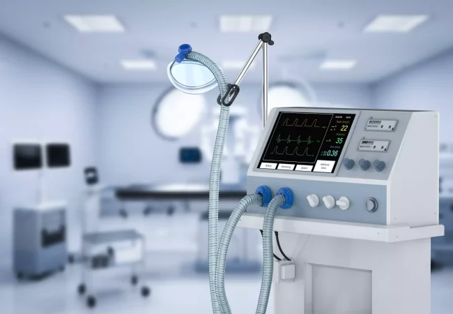 A ventilator machine displaying patient vitals in a modern, sterile operating room with blurred medical equipment in the background.