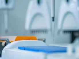 A pipette tip hovers above a blue 96-well plate, preparing for liquid dispensing during a potency assay in a laboratory setting.