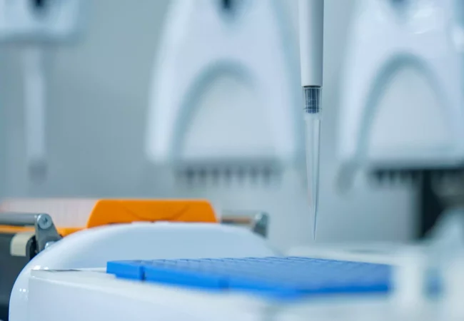 A pipette tip hovers above a blue 96-well plate, preparing for liquid dispensing during a potency assay in a laboratory setting.