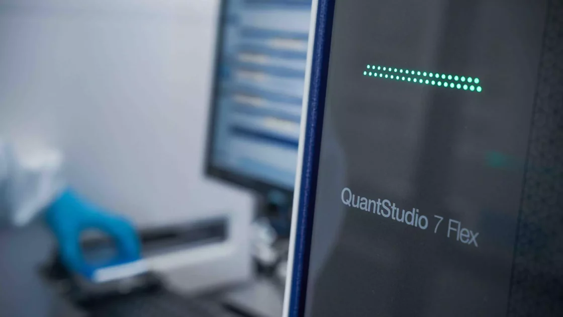 QuantStudio 7 Flex qPCR machine in use for clinical bioanalysis of large molecules, with data processing visible on a computer in the background.