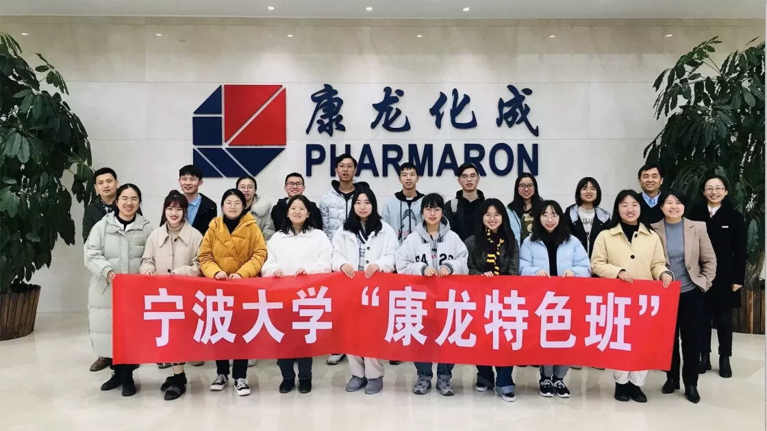 A diverse group of people, standing in front of a wall with the Pharmaron logo, are holding a red banner with Chinese characters. They are smiling and posing for the photo in a well-lit indoor space, representing expertise in Radiolabelled ADME​ and bioanalytical development.