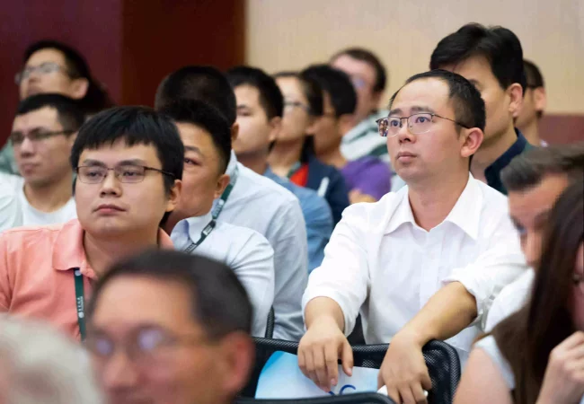 A group of professionals attentively listens during a session at the Knowledge Center, with some wearing name badges and lanyards.